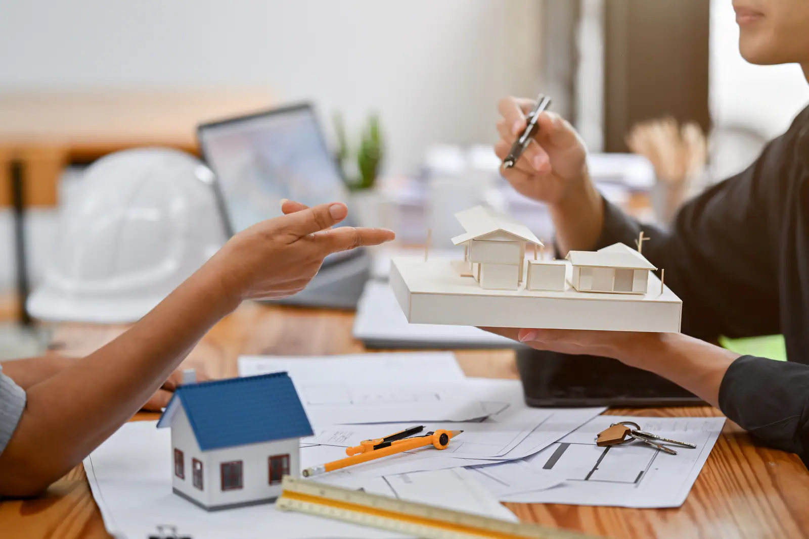 Hands over architectural plans beside a scale model of a house