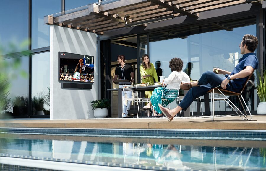 A group of people gathers for a cookout while watching a basketball game on an outdoor Samsung Terrace TV.